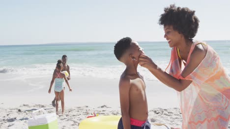 Smiling-african-american-family-using-sun-cream-on-sunny-beach