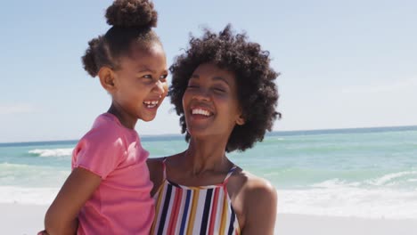 Lächelnde-Afroamerikanische-Mutter-Mit-Tochter,-Die-Sich-Am-Sonnigen-Strand-Umarmt