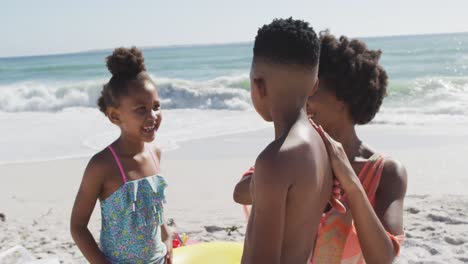 Familia-Afroamericana-Sonriente-Usando-Crema-Solar-En-La-Playa-Soleada