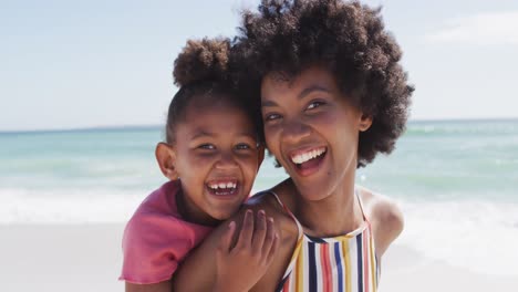 Portrait-of-smiling-african-american-mother-and-daughter-on-sunny-beach