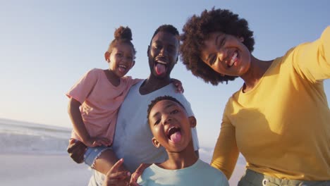 Portrait-of-smiling-african-american-family-looking-at-camera-on-sunny-beach