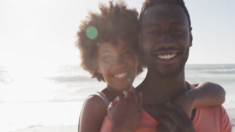 Portrait-of-smiling-african-american-couple-embracing-on-sunny-beach