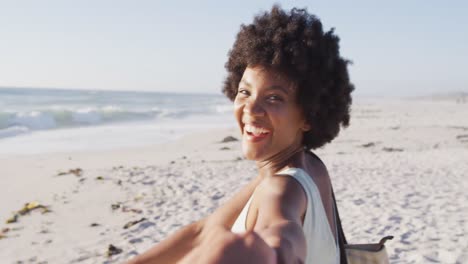 Porträt-Einer-Lächelnden-Afroamerikanischen-Frau,-Die-Hand-Am-Sonnigen-Strand-Hält