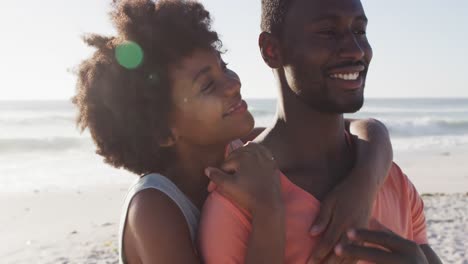 Portrait-of-smiling-african-american-couple-embracing-on-sunny-beach