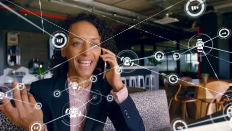Animation-of-network-of-connections-with-icons-over-biracial-businesswoman-talking-on-smartphone