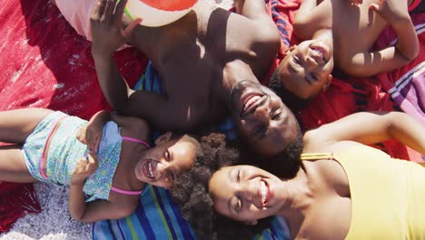 Portrait-of-smiling-african-american-family-lying-on-towels-on-sunny-beach