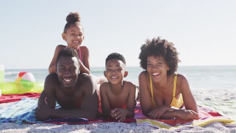 Portrait-of-smiling-african-american-family-lying-on-sunny-beach