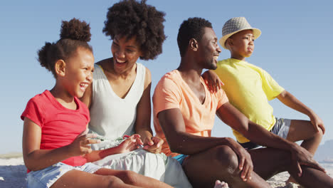 Lächelnde-Afroamerikanische-Familie,-Die-Am-Sonnigen-Strand-Sitzt-Und-Sich-Umarmt