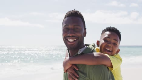 Portrait-of-smiling-african-american-father-and-son-on-sunny-beach