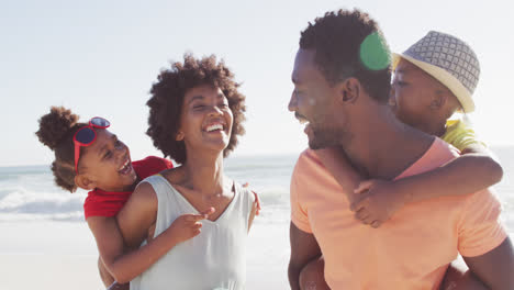 Lächelnde-Afroamerikanische-Familie,-Die-Am-Sonnigen-Strand-Trägt-Und-Umarmt