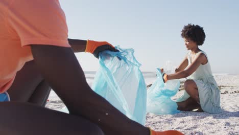 Afroamerikanisches-Paar-Trennt-Müll-Mit-Handschuhen-Am-Sonnigen-Strand