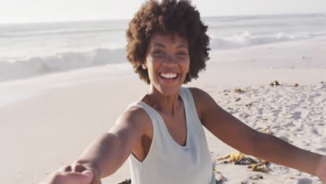 Porträt-Einer-Lächelnden-Afroamerikanischen-Frau,-Die-Hand-Am-Sonnigen-Strand-Hält