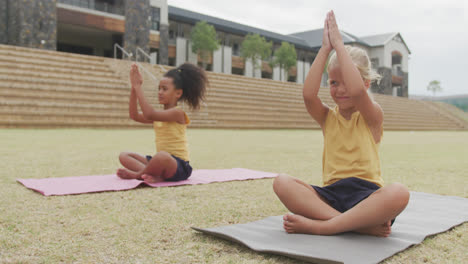 Video-of-focused-diverse-girls-practicing-yoga-on-mats-in-front-of-school
