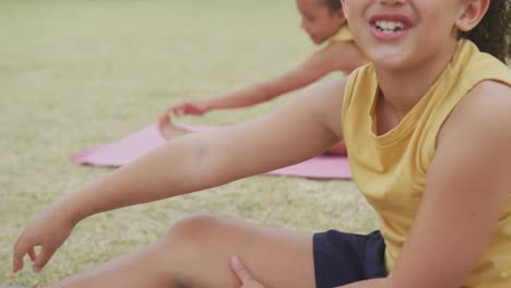Video-of-focused-diverse-girls-stretching-on-mats-in-front-of-school
