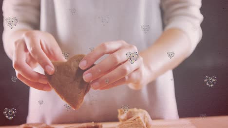 Animation-of-hearts-over-hands-of-caucasian-woman-holding-cookies