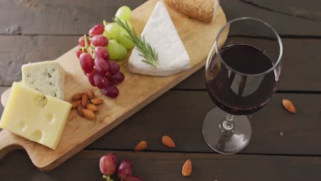 Video-of-cheeses,-bread,-grapes-and-nuts-on-board-and-glass-of-red-wine-on-wooden-table