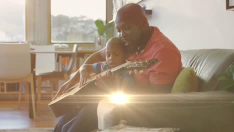 Animación-De-Puntos-De-Luz-Sobre-Un-Feliz-Padre-Afroamericano-Tocando-La-Guitarra-Con-Su-Hijo