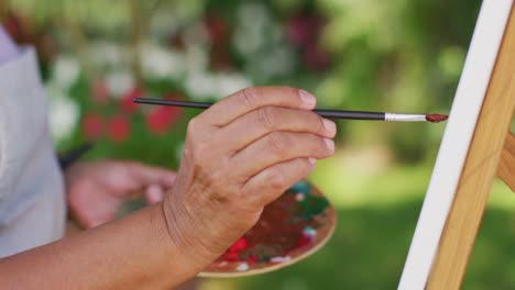 Video-of-hands-of-biracial-senior-woman-painting-in-garden