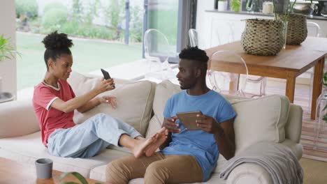 Video-of-happy-african-american-couple-sitting-on-sofa-and-using-smartphone