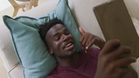 Video-Eines-Glücklichen-Afroamerikanischen-Mannes,-Der-Auf-Dem-Sofa-Liegt-Und-Einen-Videoanruf-Auf-Dem-Smartphone-Führt
