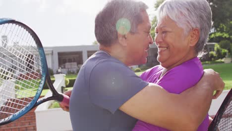 Video-Eines-Glücklichen-Gemischtrassigen-älteren-Paares,-Das-Sich-Nach-Einem-Spiel-Auf-Dem-Tennisplatz-Umarmt-Und-Küsst