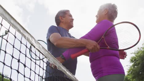Video-of-happy-biracial-senior-couple-embracing-on-tennis-court