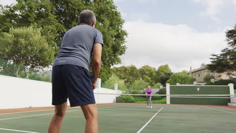 Video-of-biracial-senior-man-playing-tennis-on-tennis-court