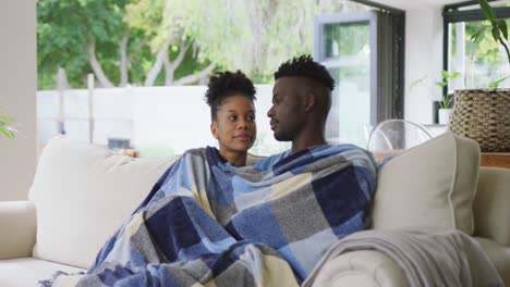 Video-of-happy-african-american-couple-sitting-on-sofa-with-blanket