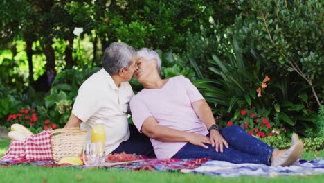 Video-of-happy-biracial-senior-couple-kissing-and-having-picnic-in-garden