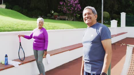 Video-Eines-Glücklichen-Gemischtrassigen-Seniorenpaares,-Das-Auf-Dem-Tennisplatz-In-Die-Kamera-Blickt