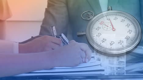 Animation-of-clock-moving-over-hands-of-caucasian-businespeople-writing