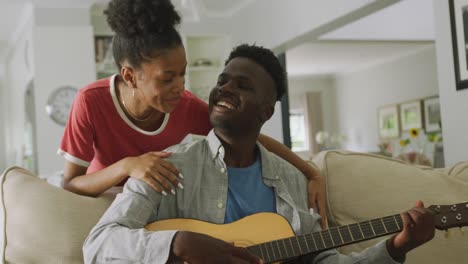 Vídeo-De-Una-Feliz-Pareja-Afroamericana-Sentada-En-El-Sofá,-Cantando-Y-Tocando-La-Guitarra