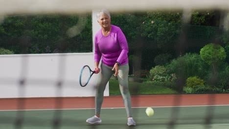 Video-Einer-Glücklichen-Biracial-Seniorin,-Die-Auf-Dem-Tennisplatz-Tennis-Spielt