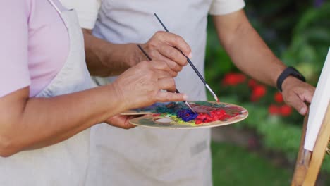 Video-of-midsection-of-biracial-senior-couple-painting-in-garden