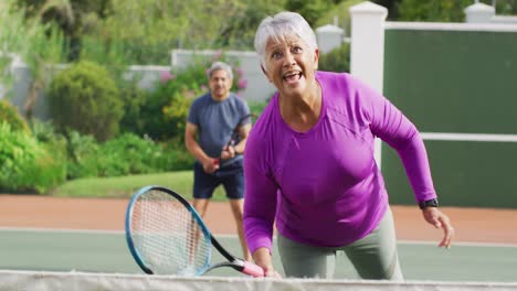 Video-of-happy-biracial-senior-woman-practicing-tennis-on-tennis-court