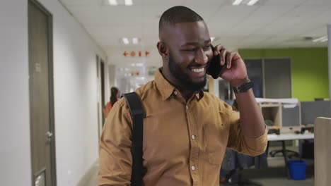 Happy-african-american-businessman-talking-on-smartphone-and-walking-in-office
