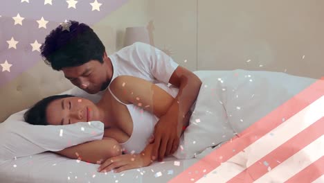 Animation-of-flag-of-usa-and-confetti-over-happy-asian-man-kissing-woman-in-bed