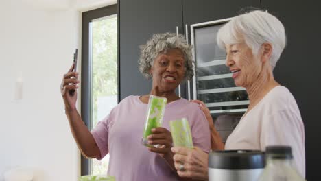 Happy-senior-diverse-women-drinking-healthy-drink-in-kitchen-at-retirement-home