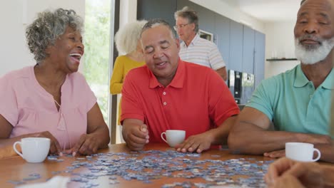 Happy-senior-diverse-people-playing-puzzle-at-table-at-retirement-home