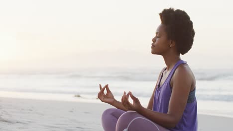 African-american-woman-practicing-yoga-and-meditating-on-sunny-beach