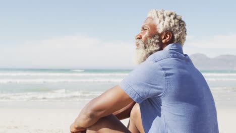 Senior-african-american-man-sitting-and-looking-away-on-sunny-beach