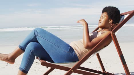 Glückliche-Afroamerikanische-Frau,-Die-Auf-Einer-Sonnenliege-Am-Sonnigen-Strand-Liegt