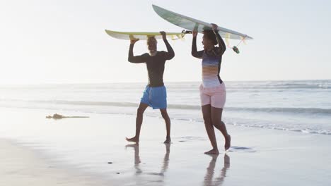 Glückliches-Afroamerikanisches-Paar,-Das-Mit-Surfbrettern-Am-Sonnigen-Strand-Spaziert