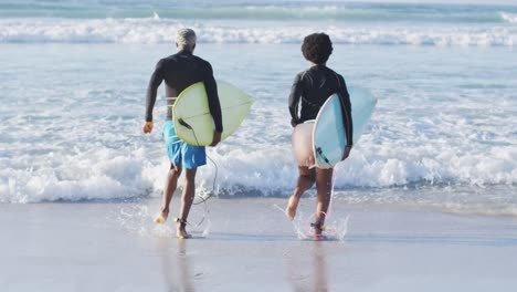 Glückliches-Afroamerikanisches-Paar,-Das-Mit-Surfbrettern-Am-Sonnigen-Strand-Läuft