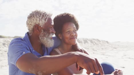Glückliches-Afroamerikanisches-Paar,-Das-Am-Sonnigen-Strand-Sitzt-Und-Sich-Umarmt