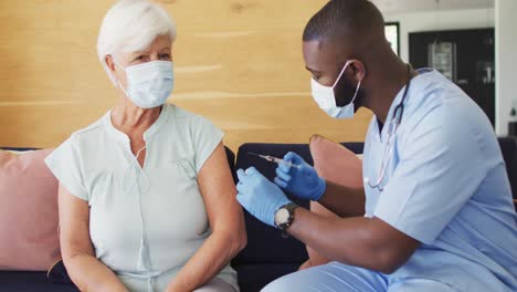 Video-Eines-Afroamerikanischen-Arztes-Mit-Gesichtsmaske,-Der-Eine-Kaukasische-Seniorin-Impft