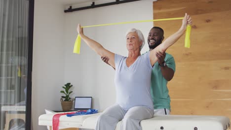 Video-Einer-Glücklichen-Kaukasischen-Seniorin,-Die-Mit-Einem-Afroamerikanischen-Physiotherapeuten-Trainiert
