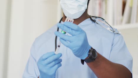 Video-Eines-Afroamerikanischen-Männlichen-Arztes-Mit-Gesichtsmaske,-Der-Den-Impfstoff-Vorbereitet