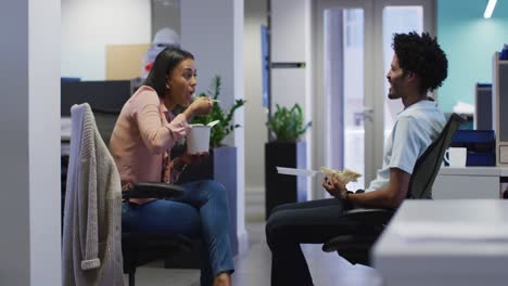 Video-of-happy-diverse-businesswoman-and-businessman-eating-and-talking-in-office