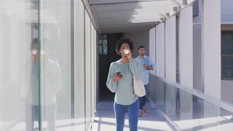 Video-of-african-american-businesswoman-walking-with-smartphone-and-coffee-in-office